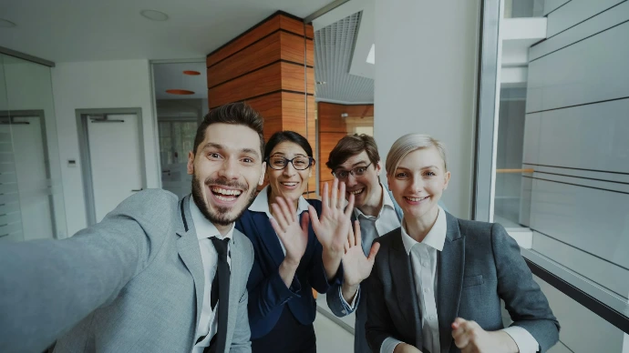 Four business people smiling and waving at camera
